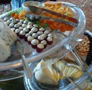 A close-up of a cheese bar with different types of cheeses, cheese knife, fork and apricots.