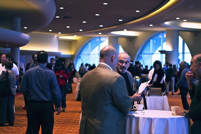 Two men having a conversation during an event in a Monona Terrace event venue. People in the background.