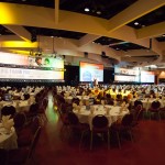 A photo taken from below angle of a meeting room with round tables and four big projector screens