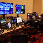 Two men from a technical crew working in the background with computers and display screens in front of them