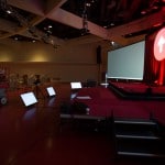 A side view of a stage and a big projector screen in a dim conference hall