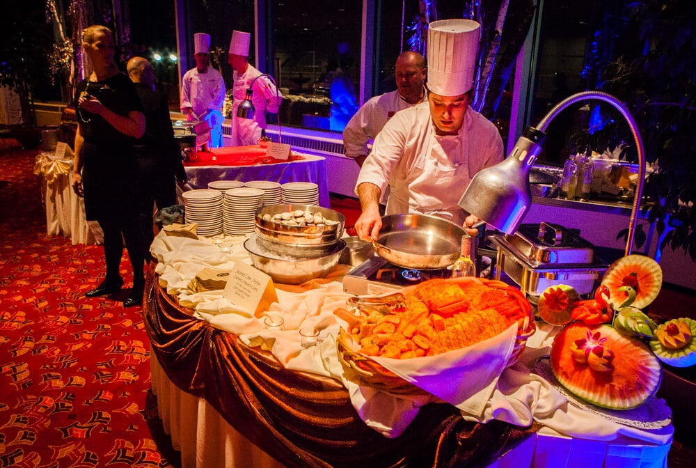 Two hot stations at a catered event with one chef heating a pot and three chefs in the background 