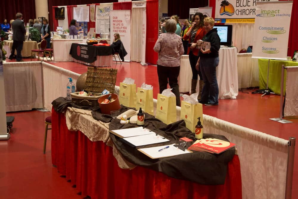 A booth at a trade fair event with sample lotion bottles, paper bags and forms on it with people in the background