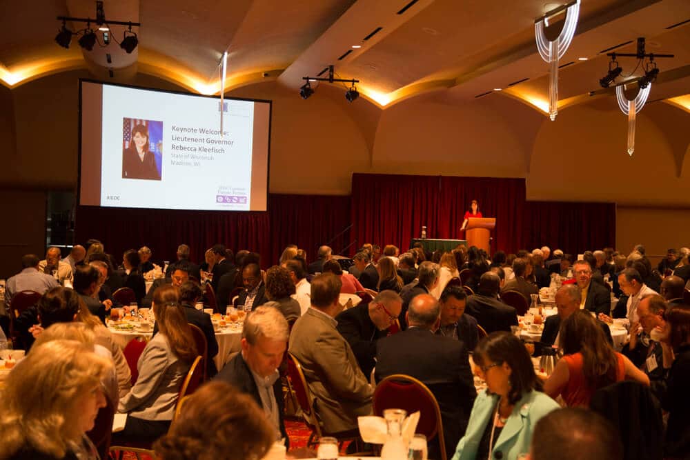 People sitting in the audience during a presentation and a speaker on the podium at the Madison Ballroom