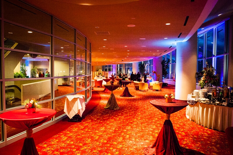 A party hall with dimmed lights, decorated tables and people at a buffet in the background