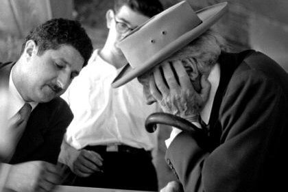 An old black-and-white photo of Frank Llyod Wright with a hat, looking at design sketches with Pedro E. Guerrero