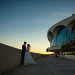 groom and bride next to a large white building