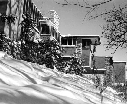 A black-and-white photograph by Guerrero of a view of a house covered in snow with trees from a lower angle.