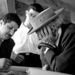 An old black-and-white photo of Frank Llyod Wright with a hat, looking at design sketches with Pedro E. Guerrero