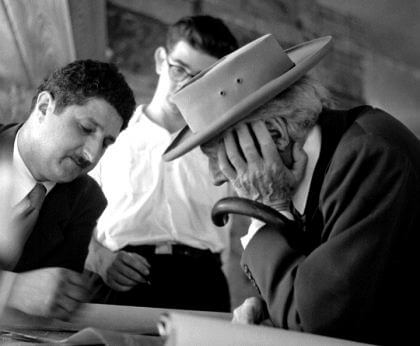 An old black-and-white photo of Frank Llyod Wright with a hat, looking at design sketches with Pedro E. Guerrero