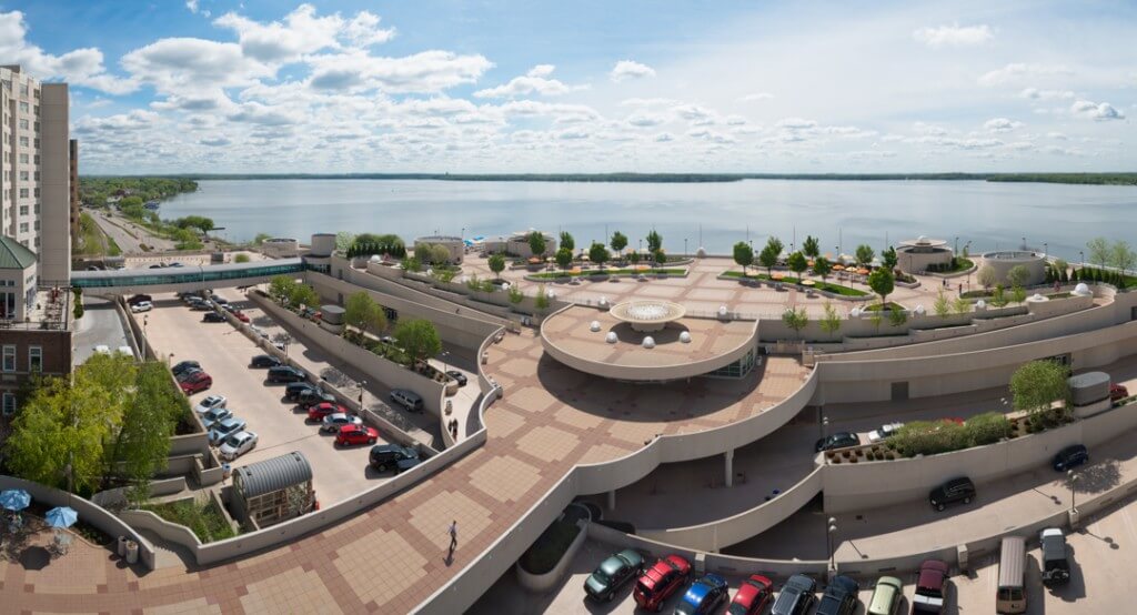 A panoramic view of William T. Evjue Rooftop Gardens by the lake with trees, and cars parked on lower levels of the building