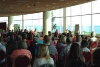 A group of people in a large meeting room with views of the lake