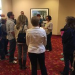 A woman talking to a group of people gathered around a painting