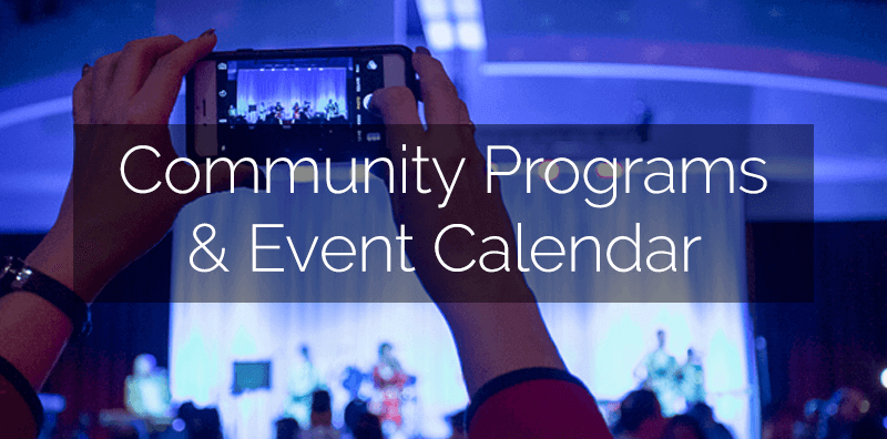 A photo of hands taking a photo of the stage during an event, with "Community Programs & Event Calendar" written on it.