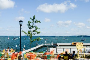 People sitting at the Memorial Union Terrace, looking at boats on Lake Mendota on yellow, orange and green chairs