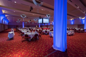 Large event room with round tables and screens from a distance