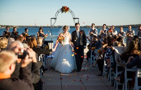 A newlywed couple walking down the aisle by the lake, as guests throw rose petals and applaud