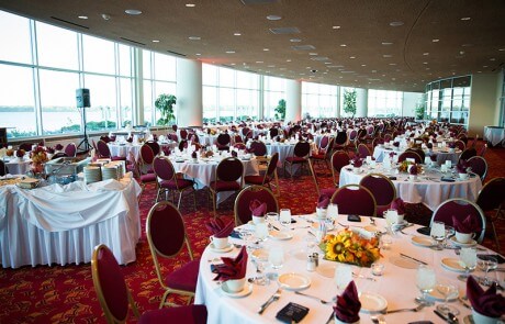 Decorated round tables at a wedding dining hall by big windows with a distant lake view