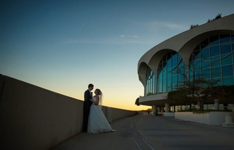 Bride and groom looking at each other, posing from a distance next to the side of Monona Terrace building by a concrete wall