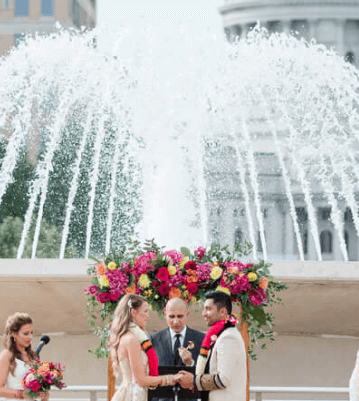 Couple getting married with a fountain and flowers in the background
