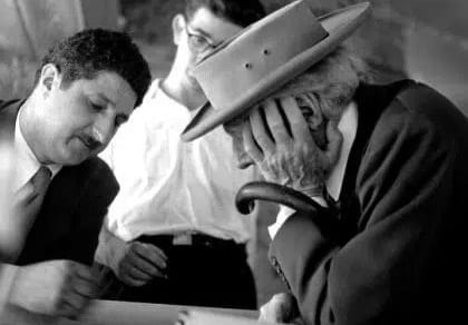 An old black-and-white photo of Frank Llyod Wright with a hat, looking at design sketches with Pedro E. Guerrero