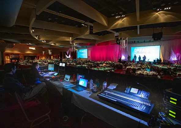 Decorated rectangular tables with red chairs in a venue with red carpet and big windows, staff working in the background
