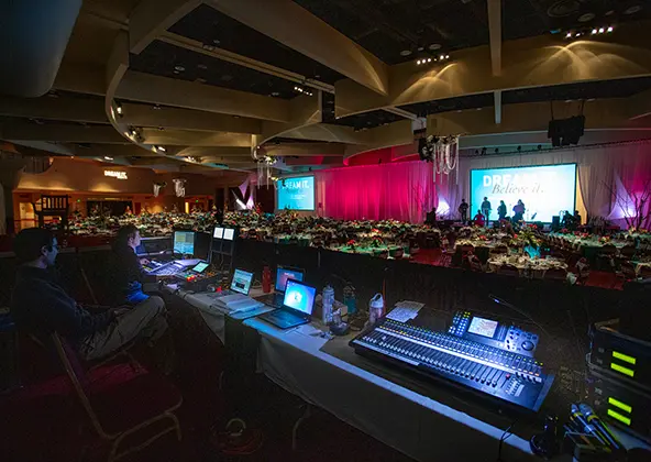 av-showcase Decorated rectangular tables with red chairs in a venue with red carpet and big windows, staff working in the background