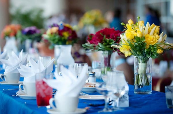 Decorated rectangular tables with red chairs in a venue with red carpet and big windows, staff working in the background