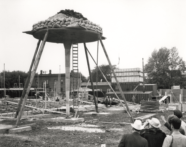 An old black-and-white photo of Frank Llyod Wright with a hat, looking at design sketches with Pedro E. Guerrero