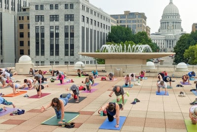 People doing yoga on the rooftop of Monona Terrace in front of a fountain with the Wisconsin State Capitol building in the background