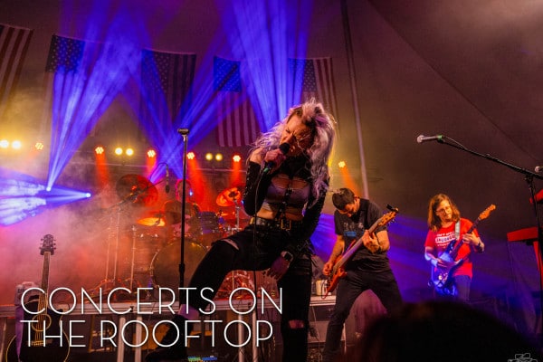 A dynamic rock band performs on a rooftop, with a charismatic singer in front. Vivid stage lights and smoke create an electrifying atmosphere.