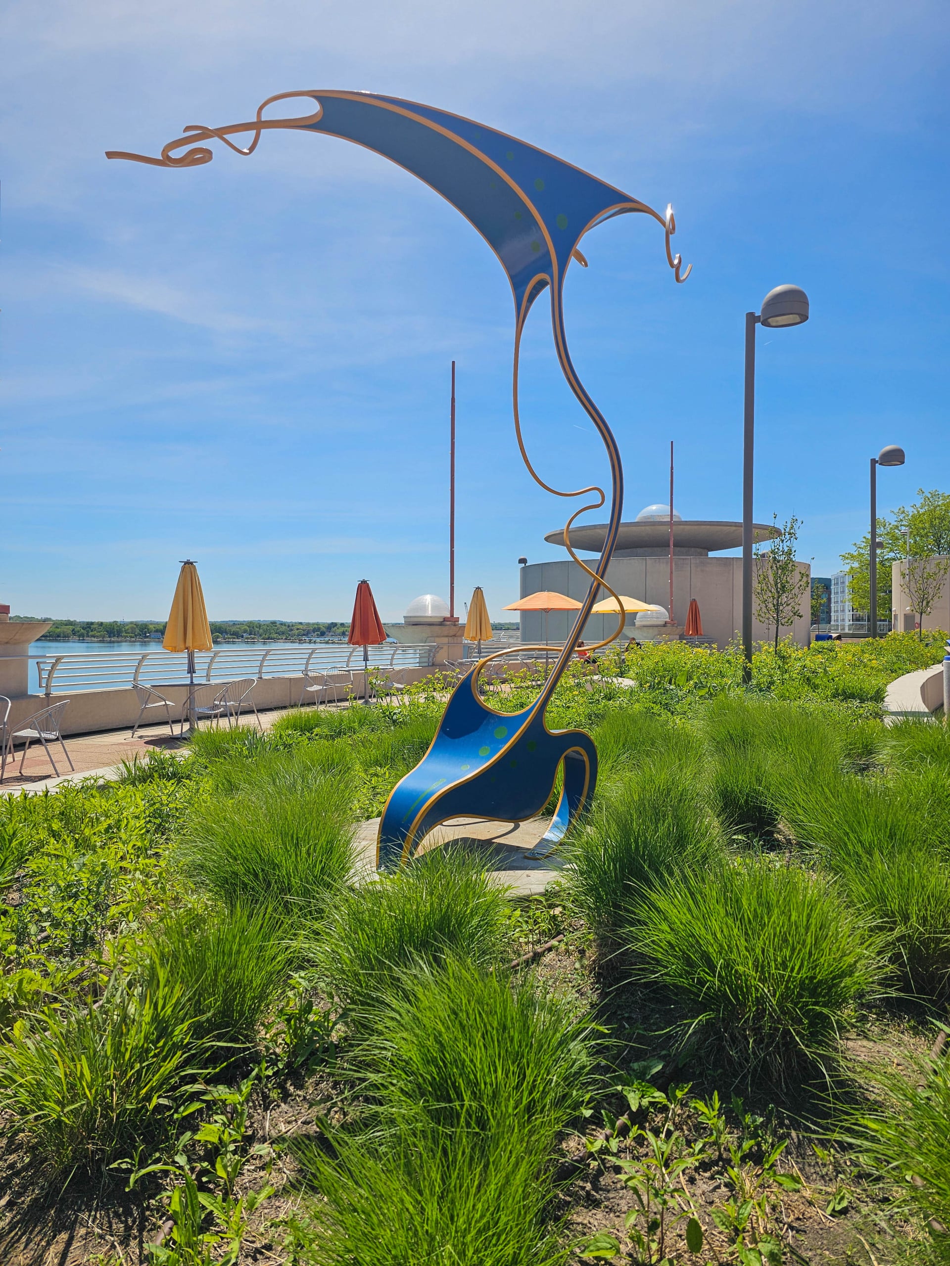 Vibrant abstract sculpture in blue and yellow with flowing lines stands near a modern entrance with a mural. Energetic and artistic urban scene.